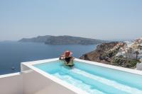 a person sitting on the edge of a swimming pool overlooking the ocean at Aspaki by Art Maisons in Oia