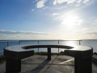 a bench in front of the ocean with the sun at Hotel et Studios Le Marina Baie de La Baule in Pornichet