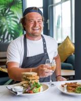 a man sitting at a table with a sandwich and a glass of wine at Oceanside Lifestyle Hotel in Newquay