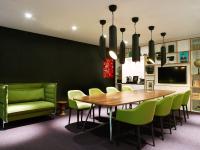 a dining room with a wooden table and green chairs at citizenM Southwark Bankside in London