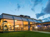 Un gran edificio de cristal con gente sentada en sillas. en Novotel Lille Aéroport, en Lesquin