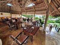 a restaurant with tables and chairs and a roof at Sunshine Bay Hotel Zanzibar in Matemwe