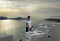 a woman standing on top of a restaurant with two tables at Tholos Resort in Imerovigli
