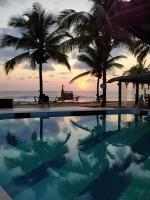 una piscina con palmeras y una persona sentada en un banco cerca de la playa en Eden One, en Ilhéus