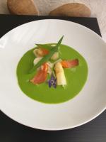 Un plato blanco con una sopa verde sobre una mesa. en Chambres et Table d'hôtes "La Pastorale Gourmande" FR - NE - EN - DE - IT, en Marcollin