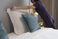 a woman standing over a bed with a pillow at Warwick Reine Astrid - Lyon in Lyon