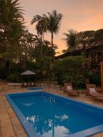 a swimming pool with palm trees and a sunset at Hotel Pousada Marambaia in Arraial d'Ajuda