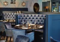 a dining room with two tables and blue booths at Formby Hall Golf Resort & Spa in Southport