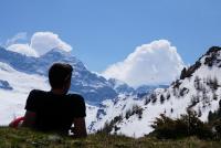 a person sitting on the grass looking at a snowy mountain at Haus Staud in Schmirn