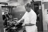 Un hombre en una cocina preparando comida en una sartén. en Hotel Lou Granva, en Grande Riviere