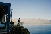 a woman standing on the balcony of a house overlooking a lake at Azur Lodge in Queenstown
