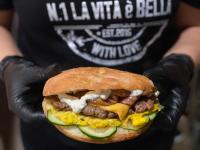 une personne portant des gants noirs tenant un hamburger dans l'établissement Paso a Paso, à Terlizzi