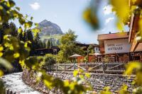 a building with a mountain in the background with yellow flowers at Hotel Gotthard in Lech am Arlberg