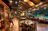 een eetkamer met tafels en stoelen en ramen bij Aahana Resort - Jim Corbett in Rāmnagar