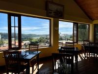 um restaurante com mesas e cadeiras e grandes janelas em Tea Bush Hotel em Nuwara Eliya