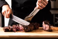 a man cutting meat on a cutting board with a knife at Ferme Delgueule in Tournai