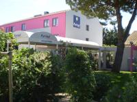a pink and white building with a tree and bushes at Kyriad Montpellier Aéroport - Gare Sud de France in Mauguio