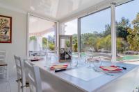 a white dining room with a long table with chairs and windows at Les Vergers in Gonfaron