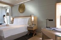 a hotel room with a bed and a woman looking out the window at Jumeirah Muscat Bay Oman in Muscat