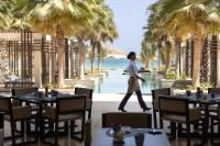 a woman walking through a restaurant with palm trees at Jumeirah Muscat Bay Oman in Muscat