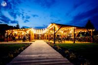 Una pasarela de madera que conduce a un pabellón con luces. en Western Camp Resort, en Zator