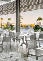 Un restaurante con mesas y sillas blancas y vista al mar. en Asterias Beach Hotel, en Ayia Napa