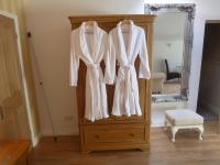 a wooden wardrobe with white coats hanging in front of a mirror at Garden Suite in Rhuddlan