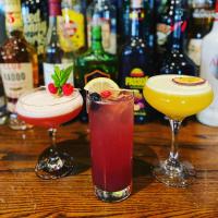 three cocktails on a wooden table with bottles of alcohol at The Valley Hotel & Carriage Gardens in Fivemiletown