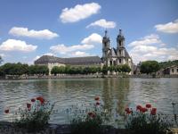 a view of a building with a lake and red flowers at Hôtel de l&#39;Abbaye des Prémontrés in Pont-à-Mousson