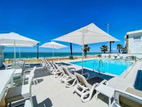 a swimming pool with white chairs and umbrellas at Hotel Apartamentos Marina Luz in Chipiona