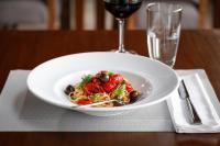 a plate of pasta with tomatoes and olives next to a glass of wine at Los Cerros del Chaltén Boutique Hotel in El Chalten