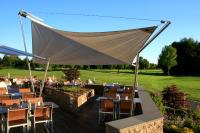 um restaurante com mesas e cadeiras debaixo de um guarda-sol branco em Golf & Resort Hotel Gut Heckenhof em Eitorf