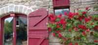 une porte rouge avec des fleurs sur un mur en pierre dans l'établissement Le refuge, à Biollet