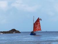 a small boat with a red sail in the ocean at Granite stone house with fireplace, Plouguerneau in Plouguerneau