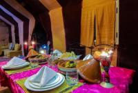 une table avec une nappe rose avec des assiettes et des bougies dans l'établissement Your magic camp, à Merzouga