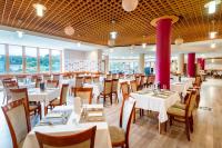 Un restaurante con mesas y sillas blancas y ventanas. en Hunguest Hotel Pelion, en Tapolca