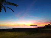 a sunset on the beach with a palm tree at Casa Las Toro Playa in Chilches