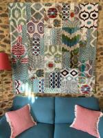 a quilt hanging above a blue couch with pink pillows at Gîte Maison Maitri in Forgès