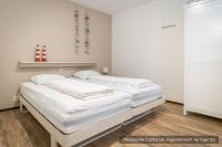 two beds in a room with white walls and wood floors at Residentie Californië in De Koog