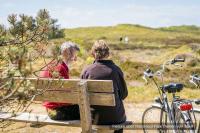 two people sitting on a bench next to a bike at Residentie Californië in De Koog
