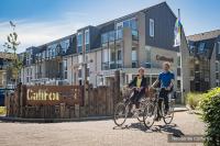 two people riding their bikes in front of buildings at Residentie Californië in De Koog