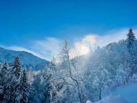 a snow covered forest with a rainbow in the sky at Le Chalet de Bémont in Samoëns