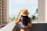 a woman wearing a hat looking out a window at Hotel Renew in Honolulu