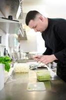 un hombre de pie en una cocina preparando comida en The Originals Boutique, Hôtel La Colonne de Bronze, Saint-Valéry-sur-Somme, en Saint-Valery-sur-Somme