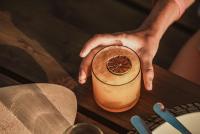 Eine Hand hält ein Getränk auf einem Holztisch in der Unterkunft The Salty Surf & Yoga in Monte Estoril