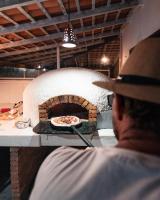 Een man maakt een pizza in een pizzaoven. bij Beekite Wind Village in Luis Correia