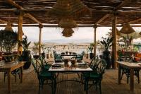 マラケシュにあるCaravan Agafay by Our Habitasのビーチの景色を望むレストラン(テーブル、椅子付)