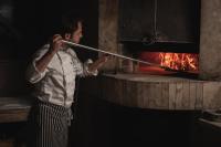 Ein Mann hält eine Stange vor einem Feuerofen in der Unterkunft Hotel Borovi Forest Resort & Spa in Sjenica