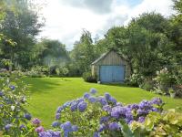 an old shed in a garden with purple flowers at Charming holiday home with garden in Huelgoat