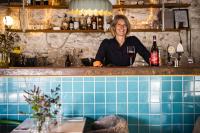 una mujer de pie detrás de una barra con una copa de vino en Grå Gåsen, en Burgsvik